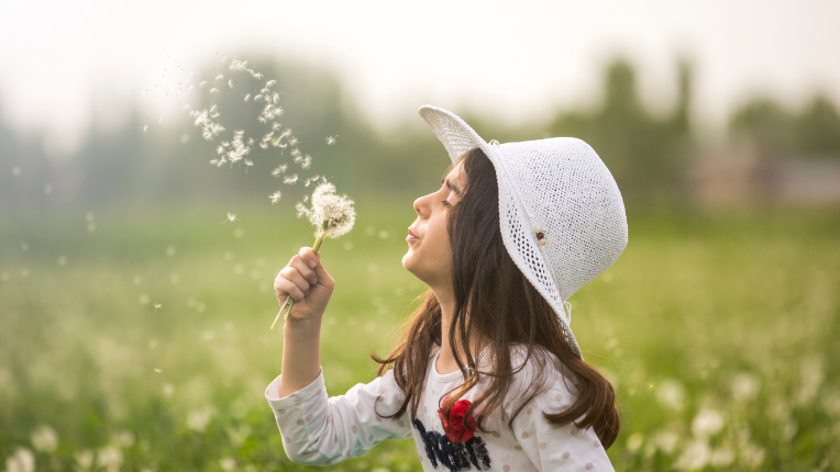 A girl blowing dandelion in a garden