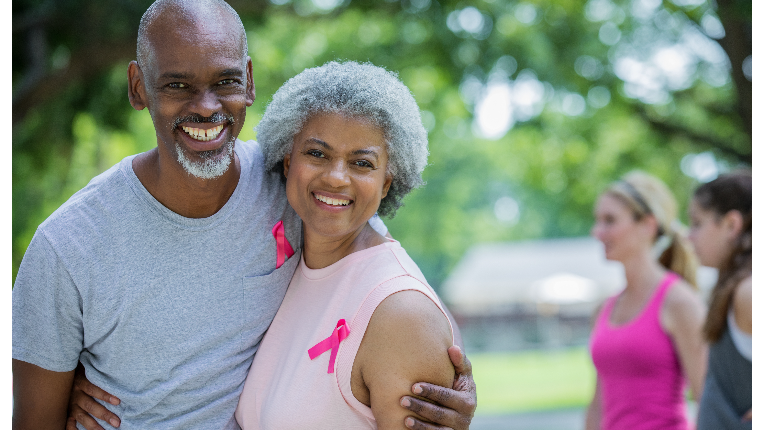 Mature couple smiling in athletic attire and while wearing pink ribbons.