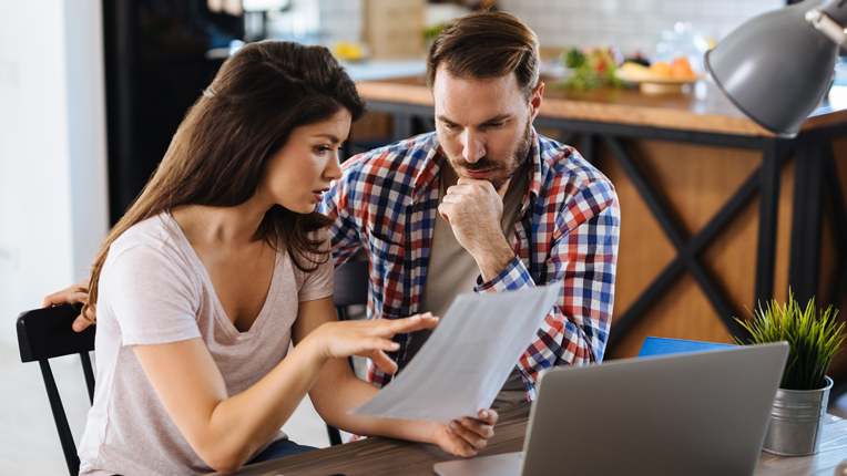 2. A couple sitting at the kitchen table looking at a sheet of paper in front of an open computer