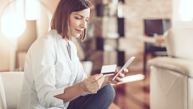 1. A woman sitting in a living room sitting on a white couch with a card in one hand and a phone in the other