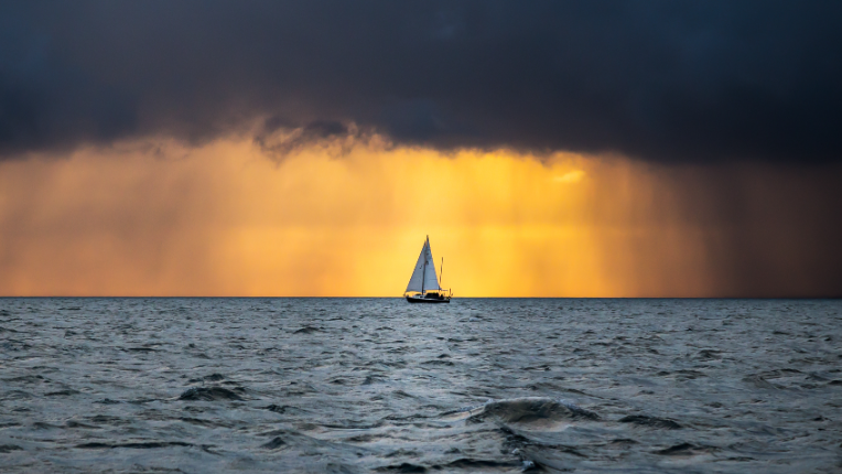 A dark cloud over a boat in the middle of the ocean.