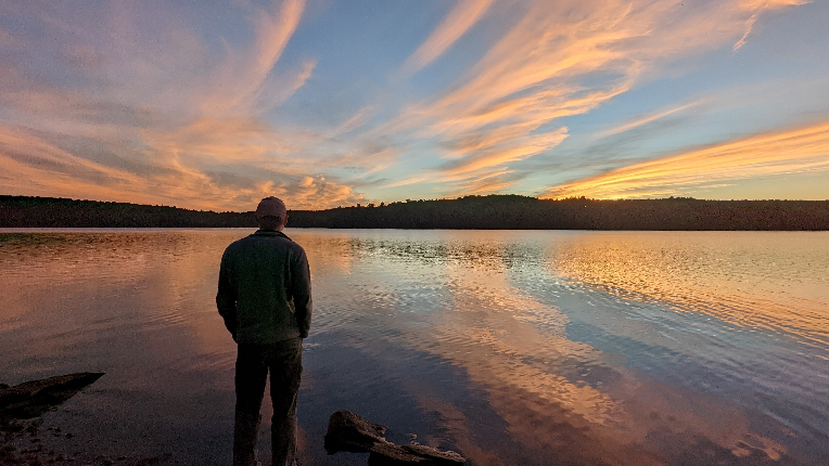 A silhouette of a man watching a sunset over a lake.