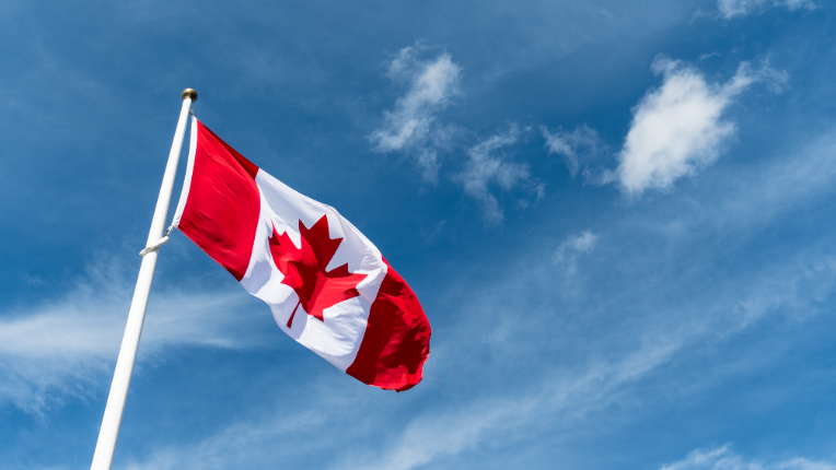 Canadian flag blowing in the wind front of clear blue sky.