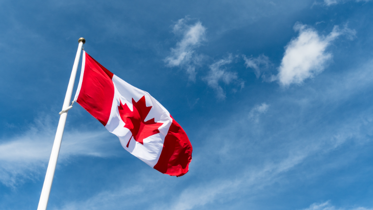 Canadian flag blowing in the wind in front of clear blue sky.