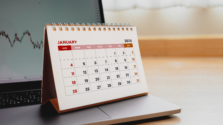 Calendar of January 2026 on top of laptop with market numbers in background.