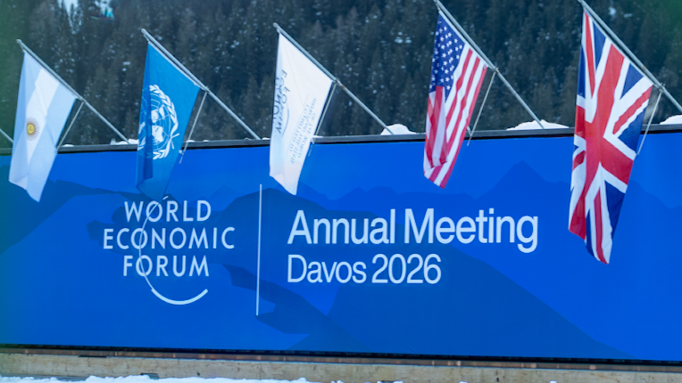 A sign at the World Economic Forum Annual Meeting in Davos, Switzerland showing its logo. The flag of Argentina, the United Nations, the United States of America, the United Kingdom, and Italy hang over the sign.