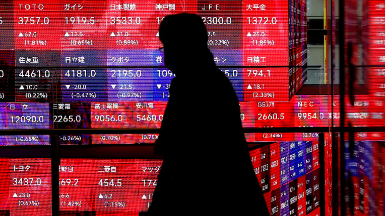 A visitor walks past Japan's Nikkei stock prices quotation board