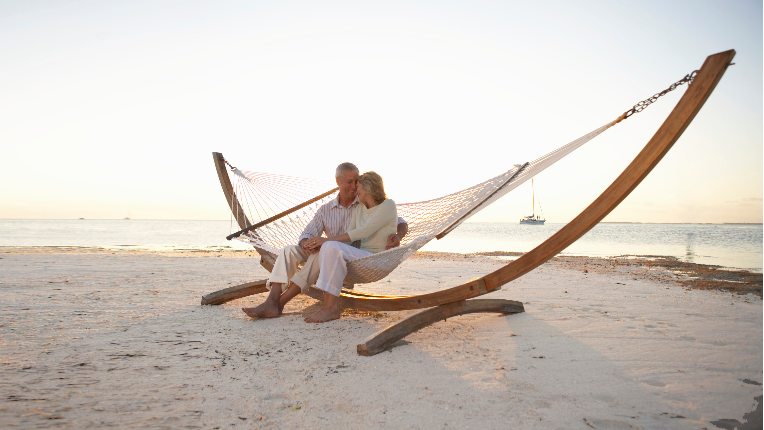 Mature couple sitting on hammock on beach, heads together