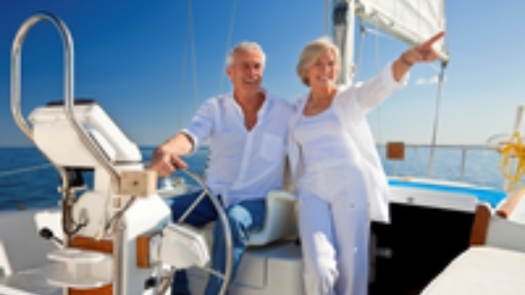 older couple on a sailboat with the woman pointing to the distance.