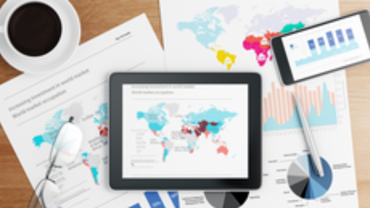 Phone, tablet and coffee on a table of papers with graphs on them