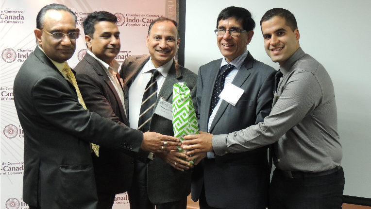 Avin, Peter and other people holding a gift together at Indo-Canada Chamber of Commerce event.