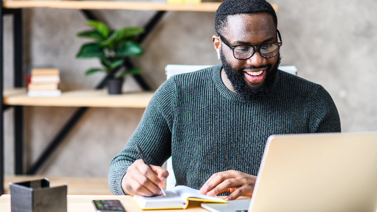 A young man smiling and working on a laptop in a modern office.