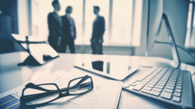 three business people in suits in the background of a tablet, a keyboard and some glasses on a table