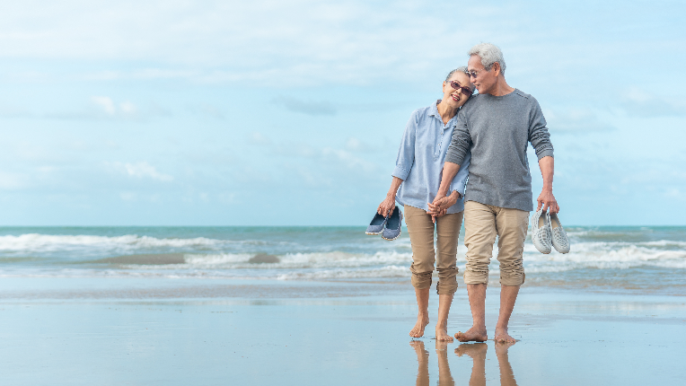 Happy senior couple holding hands and walking on beach.