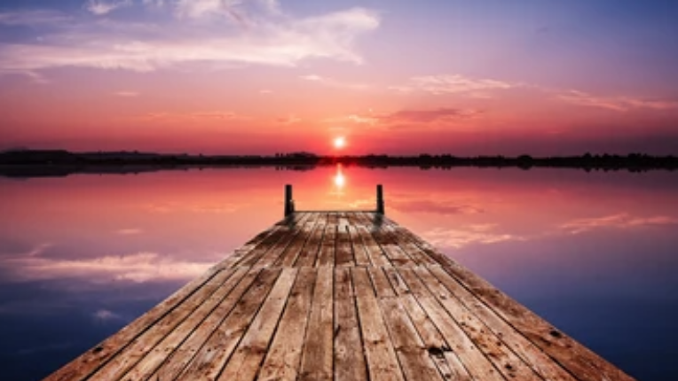 The view of a lake from a dock at sunset.
