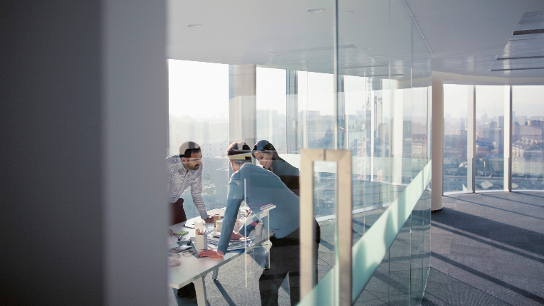 three people standing around a table in an office of windows