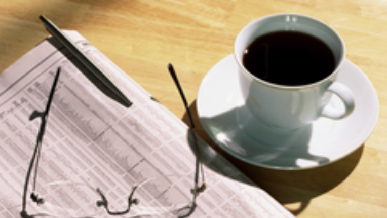 a newspaper with glasses lying on top and a cup of coffee beside