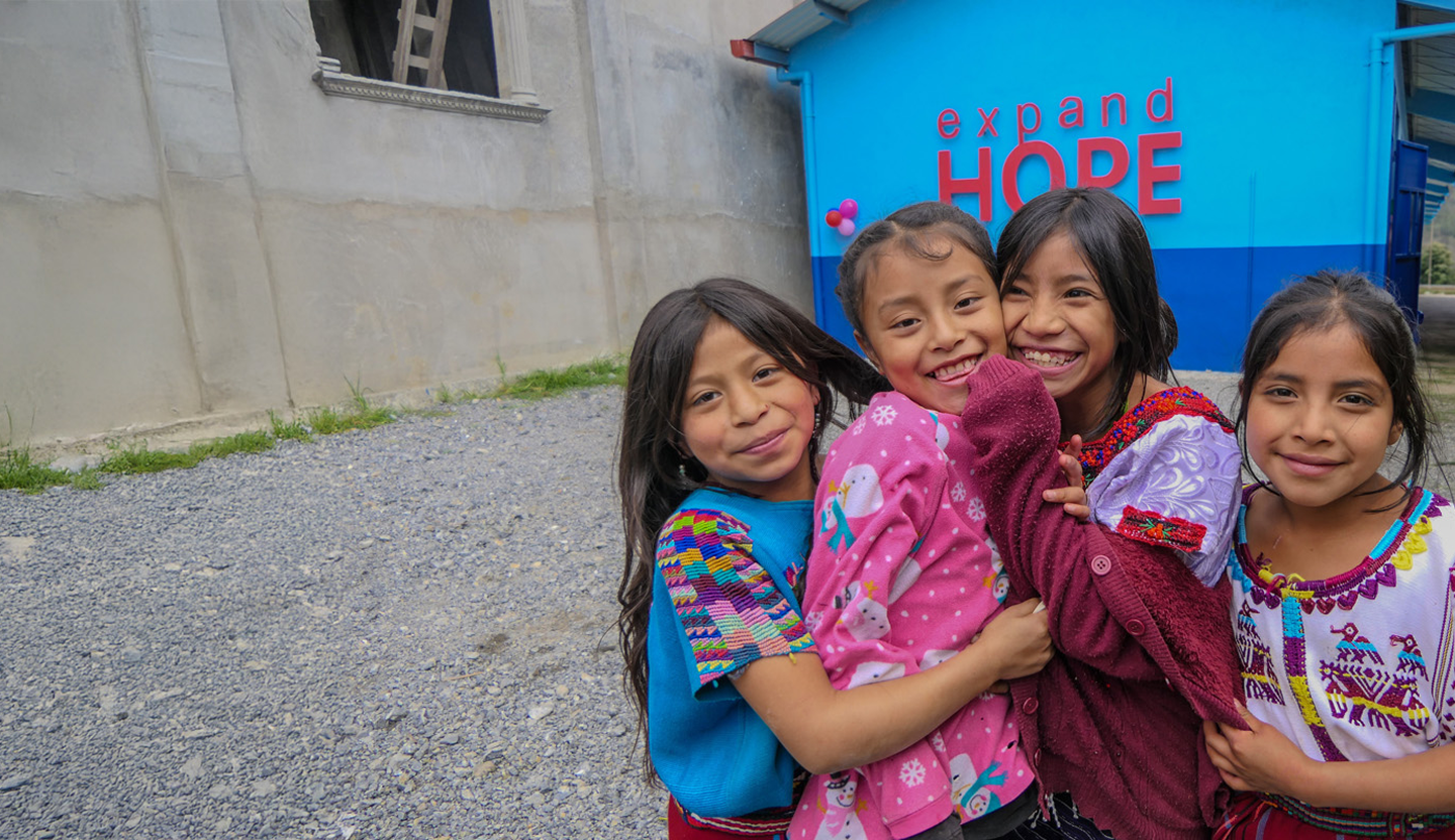 A group of children standing together outside in front of a bright blue building with the words 