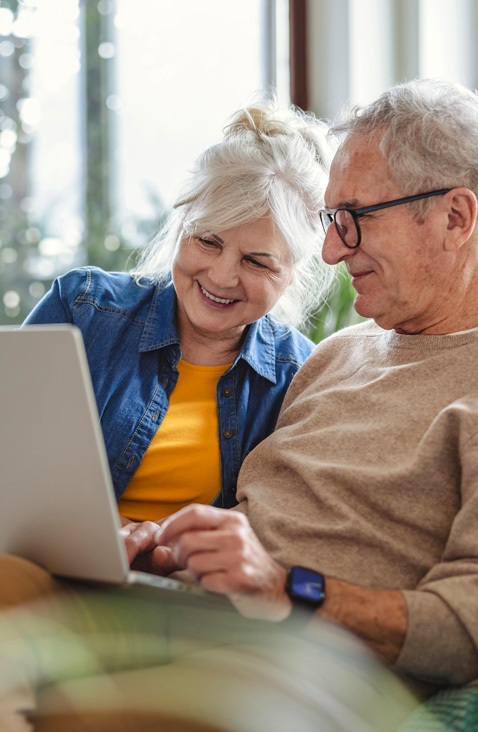 Older couple sitting together on a couch using a laptop.