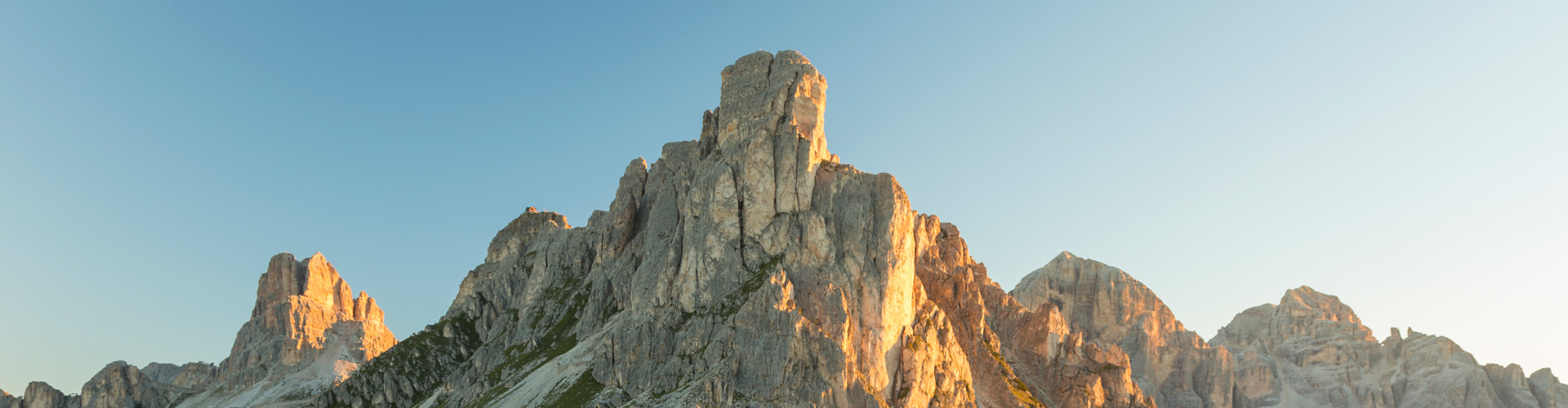 Dramatic rocky mountain cliffs glowing in warm light beneath a clear blue sky.