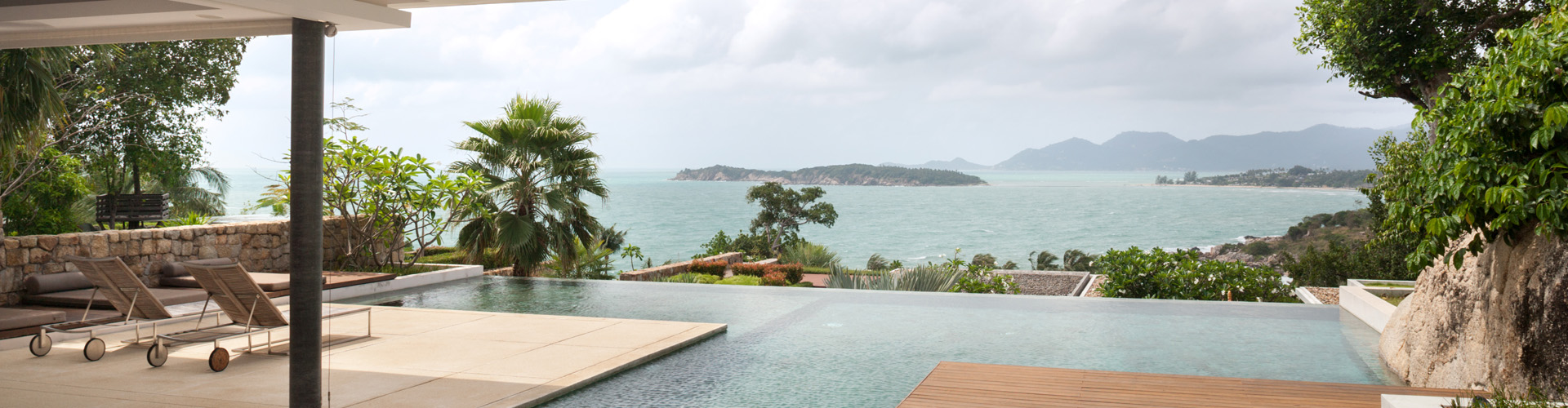Luxury seaside terrace with lounge chairs and an infinity pool overlooking tropical islands and calm ocean water.