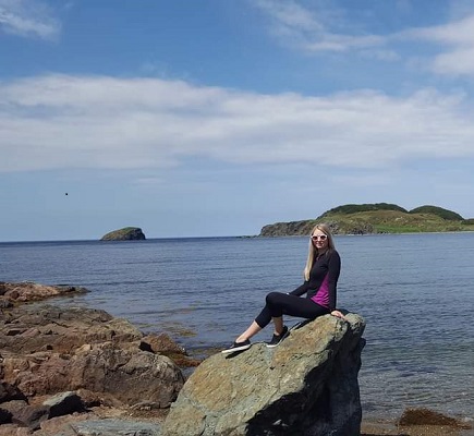 Mara draper sitting on a rock beside an ocean