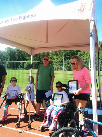 Sandra Dyck smiling with two children in wheel chairs at the Run Walk and Roll community event